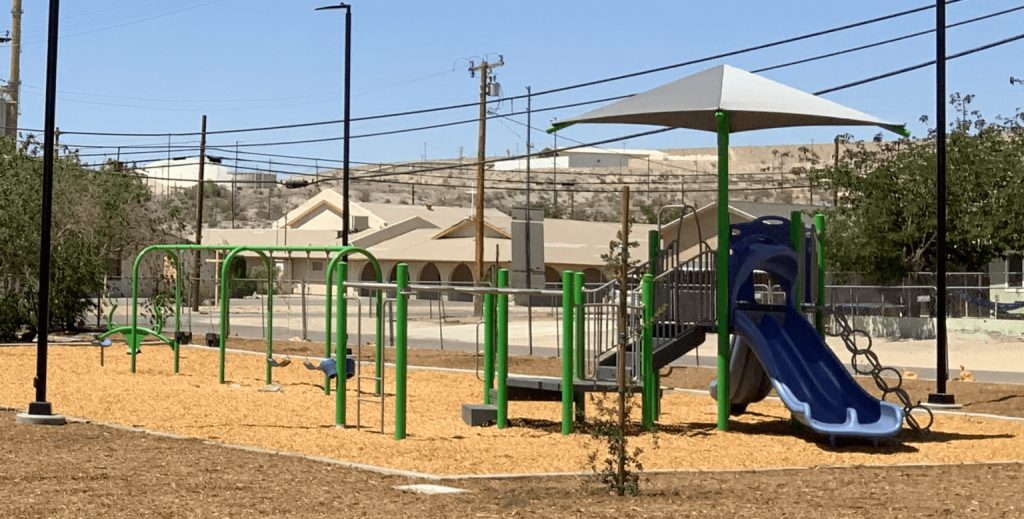 New playground features swings, climbing elements, and a shaded slide area for kids in a desert community park.