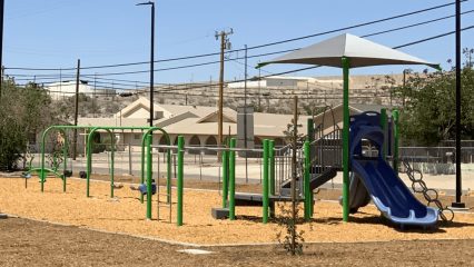 New playground features swings, climbing elements, and a shaded slide area for kids in a desert community park.