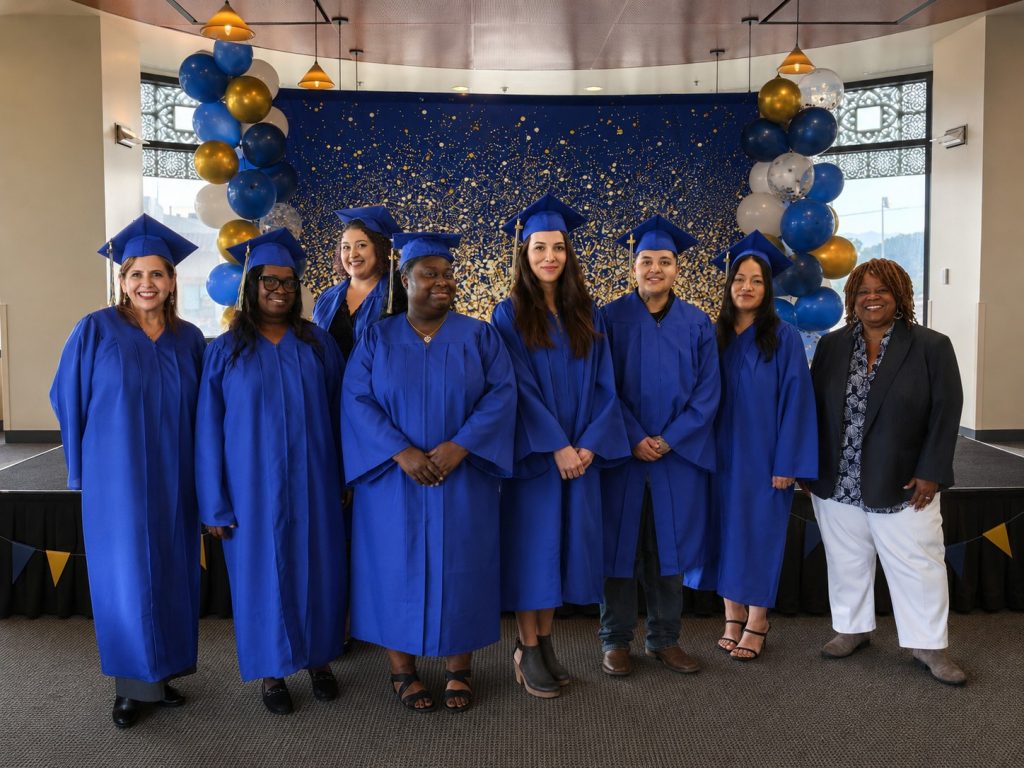Seven graduates and one faculty member celebrate their achievements against a starry backdrop accented with festive blue and gold balloons.