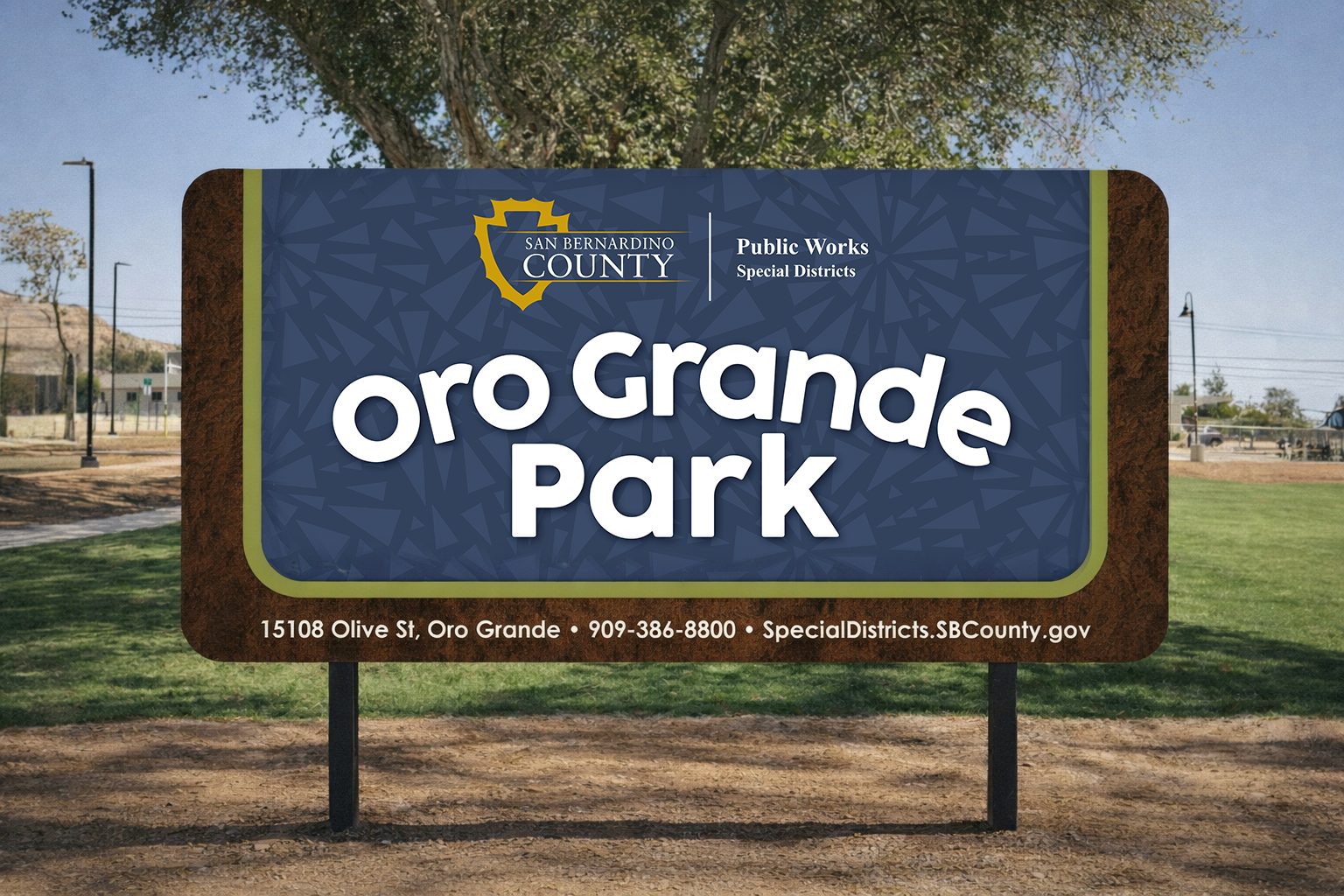 Tree behind Sign in a park that reads: San Bernardino County Public Works Special Districts. Oro Grande Park. 15108 Olive St, Oro Grande • 909-386-8800 • SpecialDistricts.SBCounty.gov