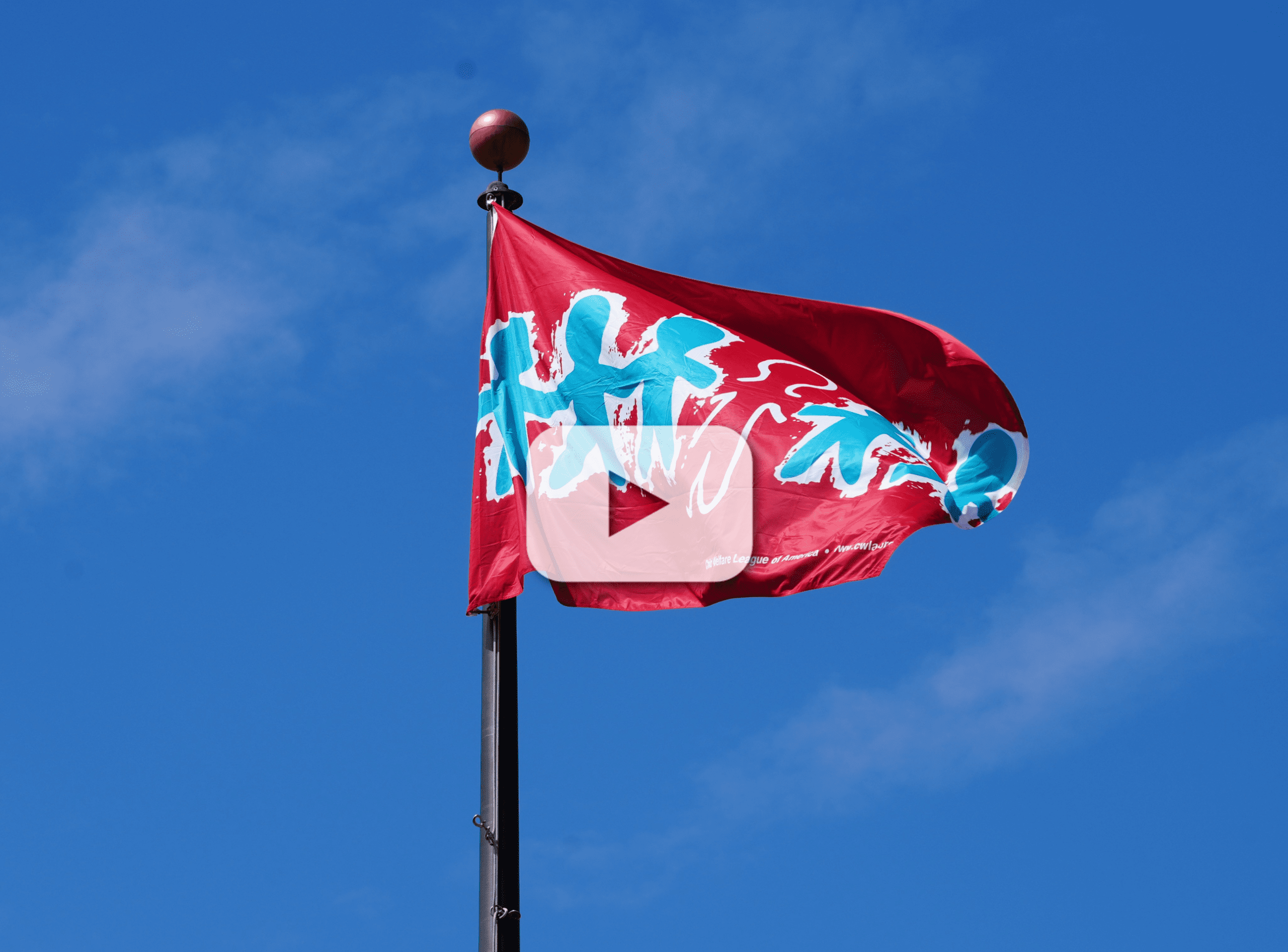 Red flag with teal human figures waves on a flagpole against a clear blue sky.