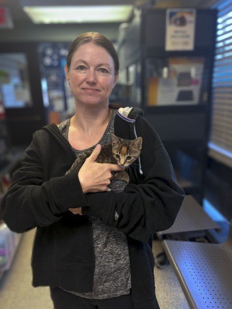 A woman standing inside an animal shelter, holding a small kitten. 