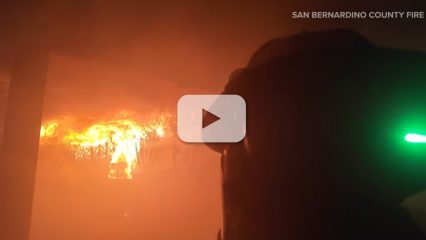 A firefighter stands away from a wall of flames with a video play button.