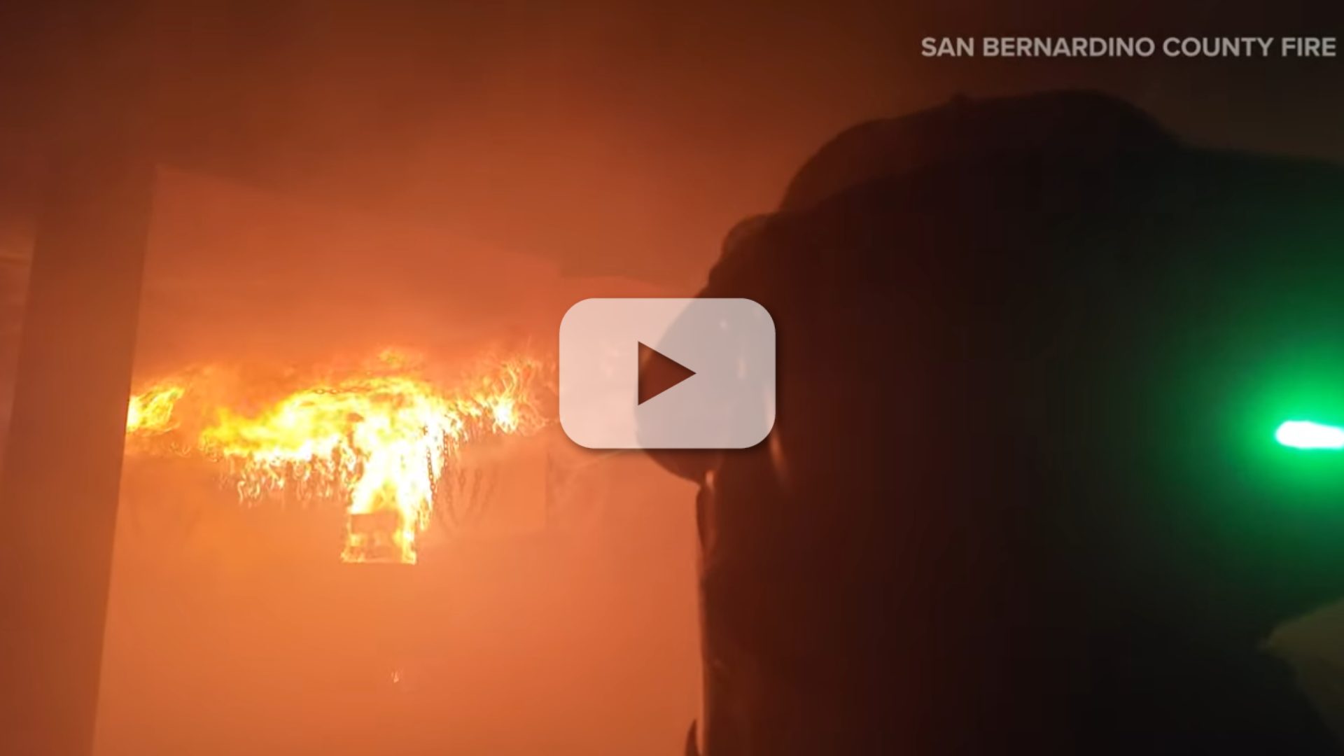 A firefighter stands away from a wall of flames with a video play button.