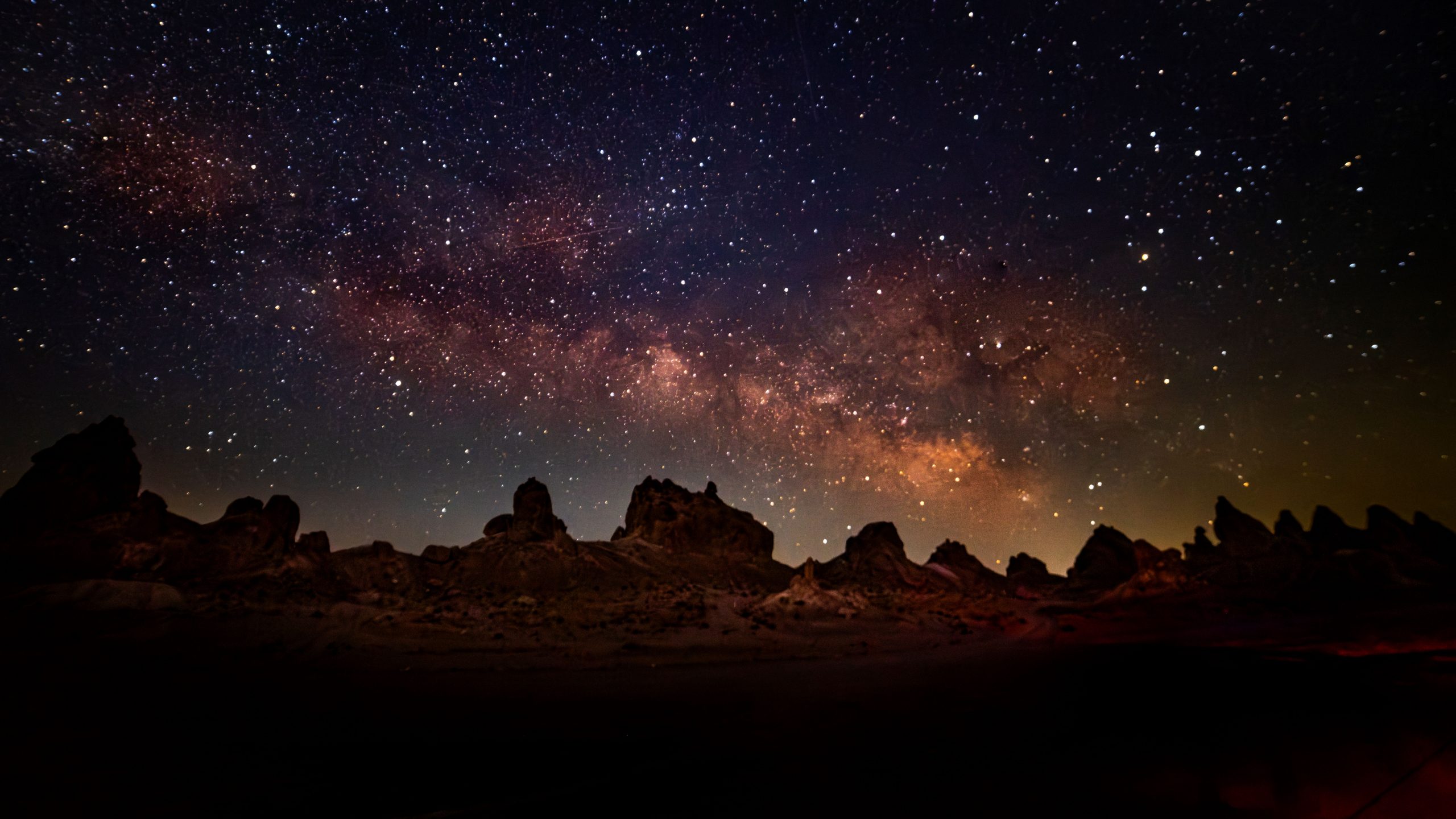 A nighttime view of Trona Pinnacles under a star-filled sky with visible Milky Way galaxy.