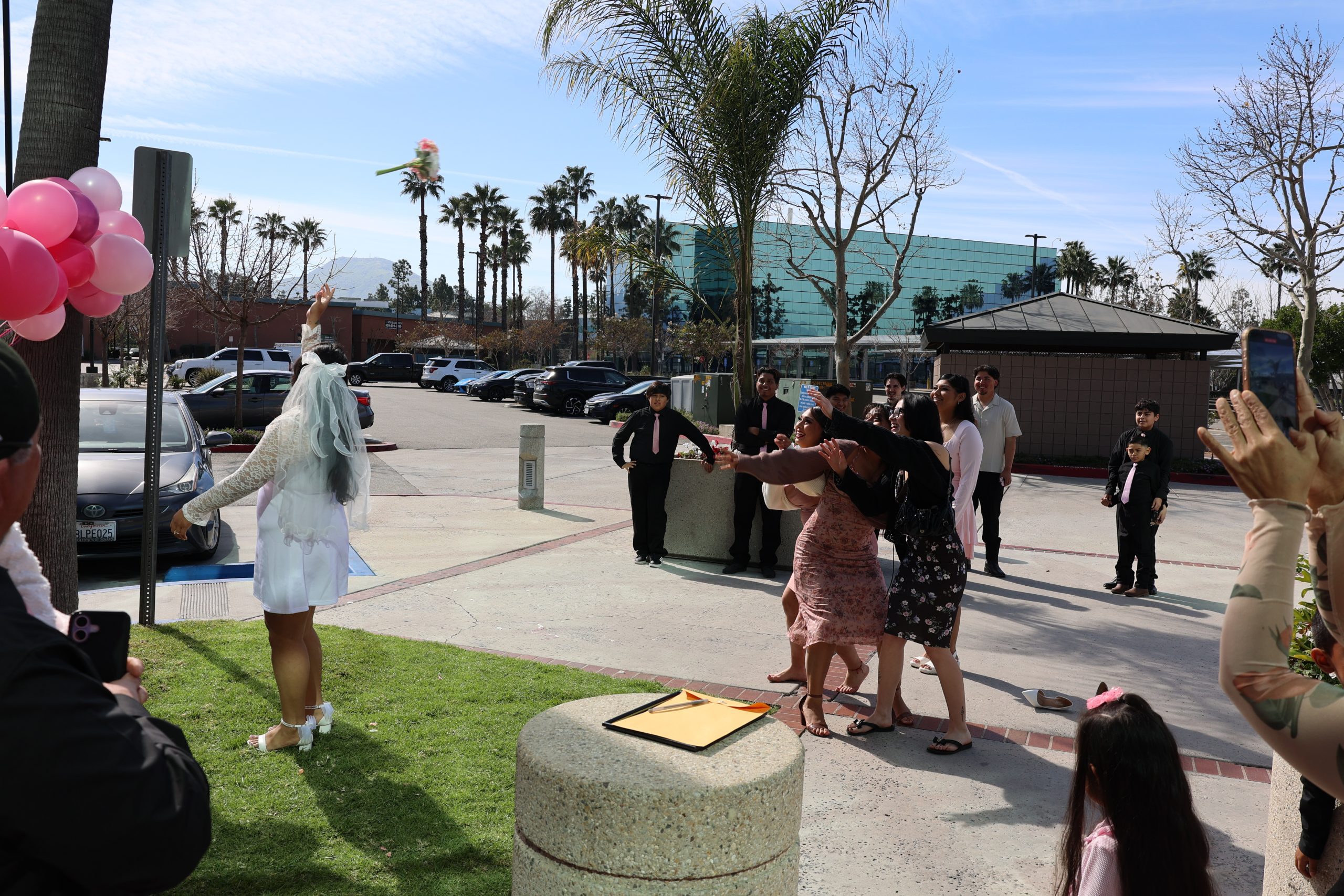 Bride tossing her bouquet to a group of excited women reaching to catch it.