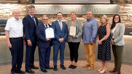 Eight people pose together indoors at East Valley Water District, with two individuals holding certificates of recognition.