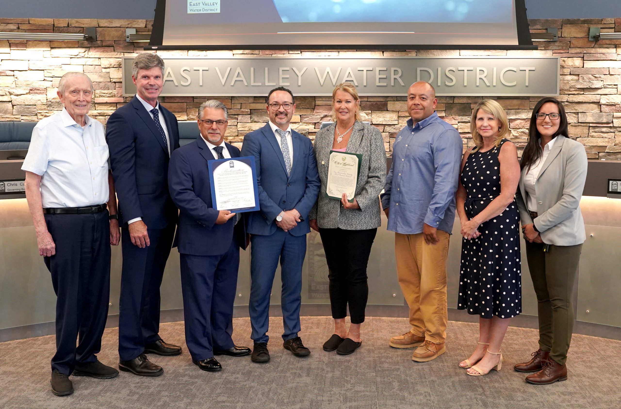 Eight people pose together indoors at East Valley Water District, with two individuals holding certificates of recognition.