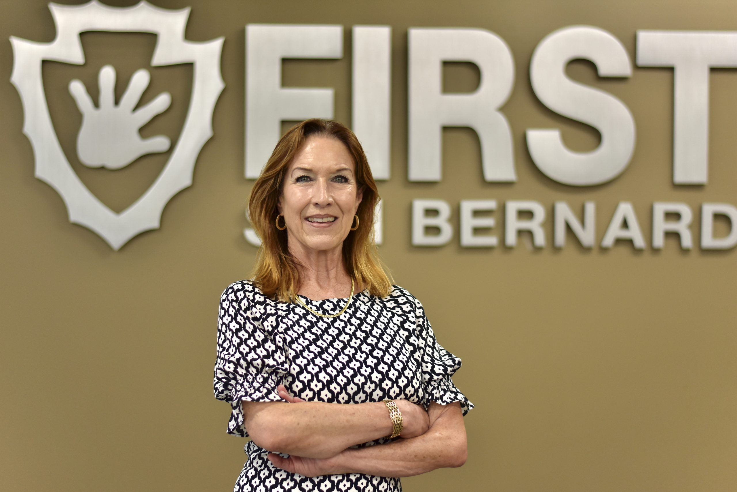 A person stands in front of a wall with the text "First San Bernardino" and an arrowhead logo featuring a handprint.