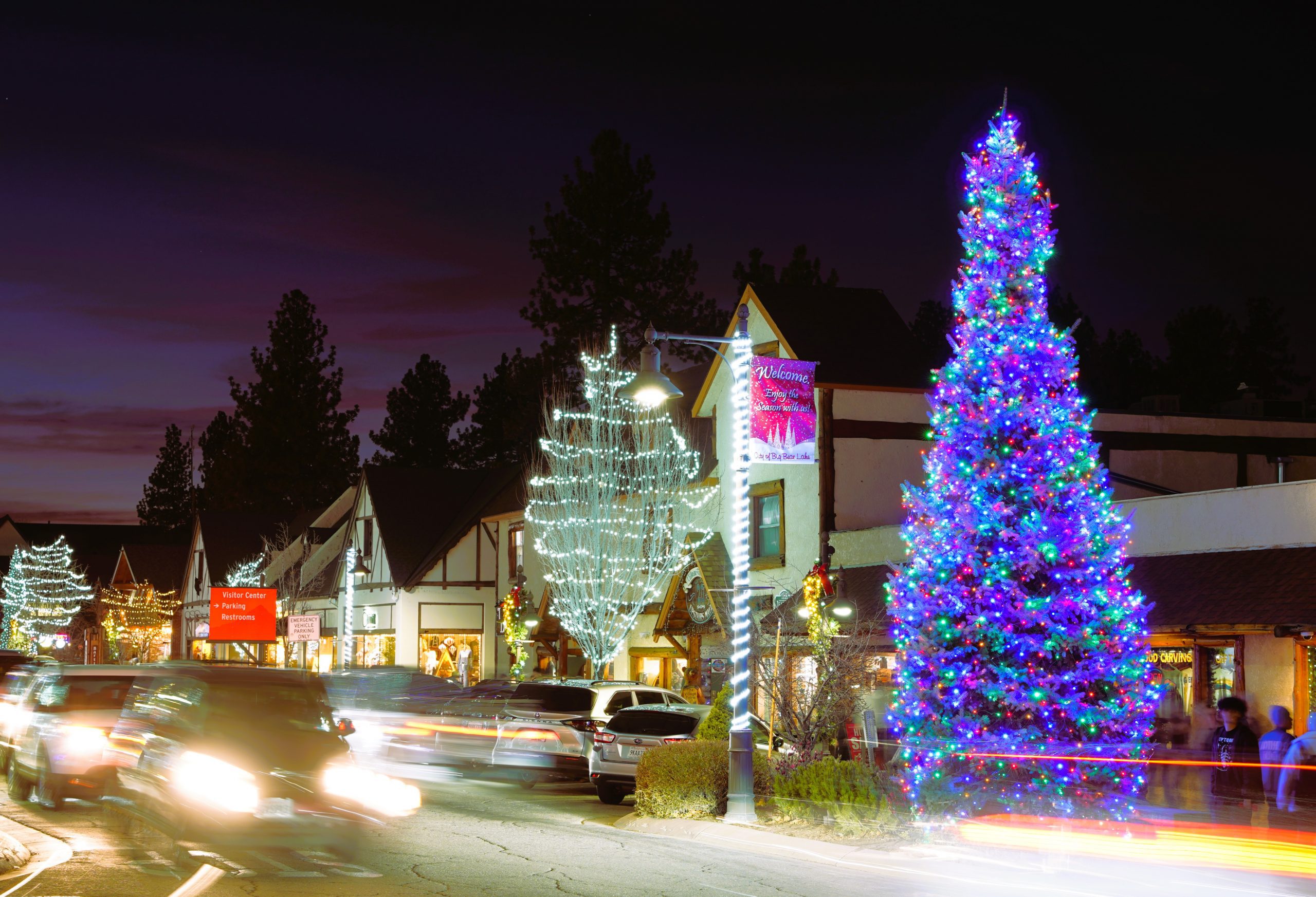 An illuminated Christmas tree with colorful lights positioned next to a carved wooden bear sculpture.
