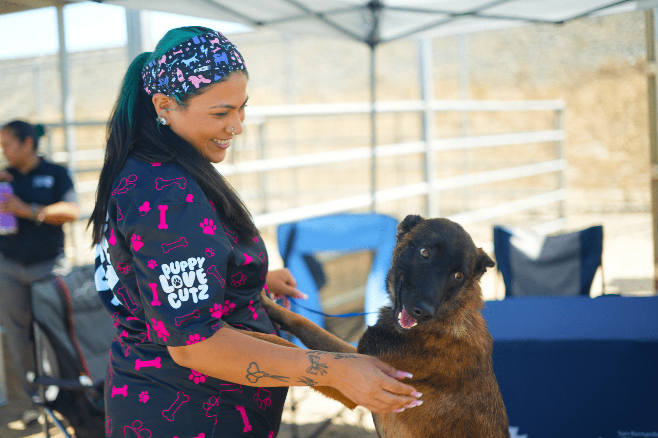 A groomer stands under a canopy with a dog on a leash, the dog looking up with a friendly expression.