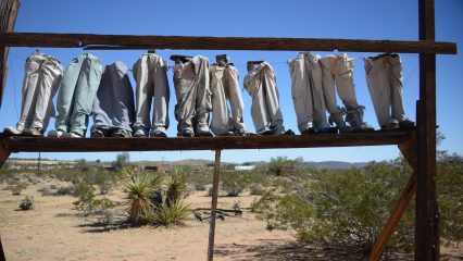 An art piece featuring a row of jeans and shoes hanging from a wooden rack in the desert.