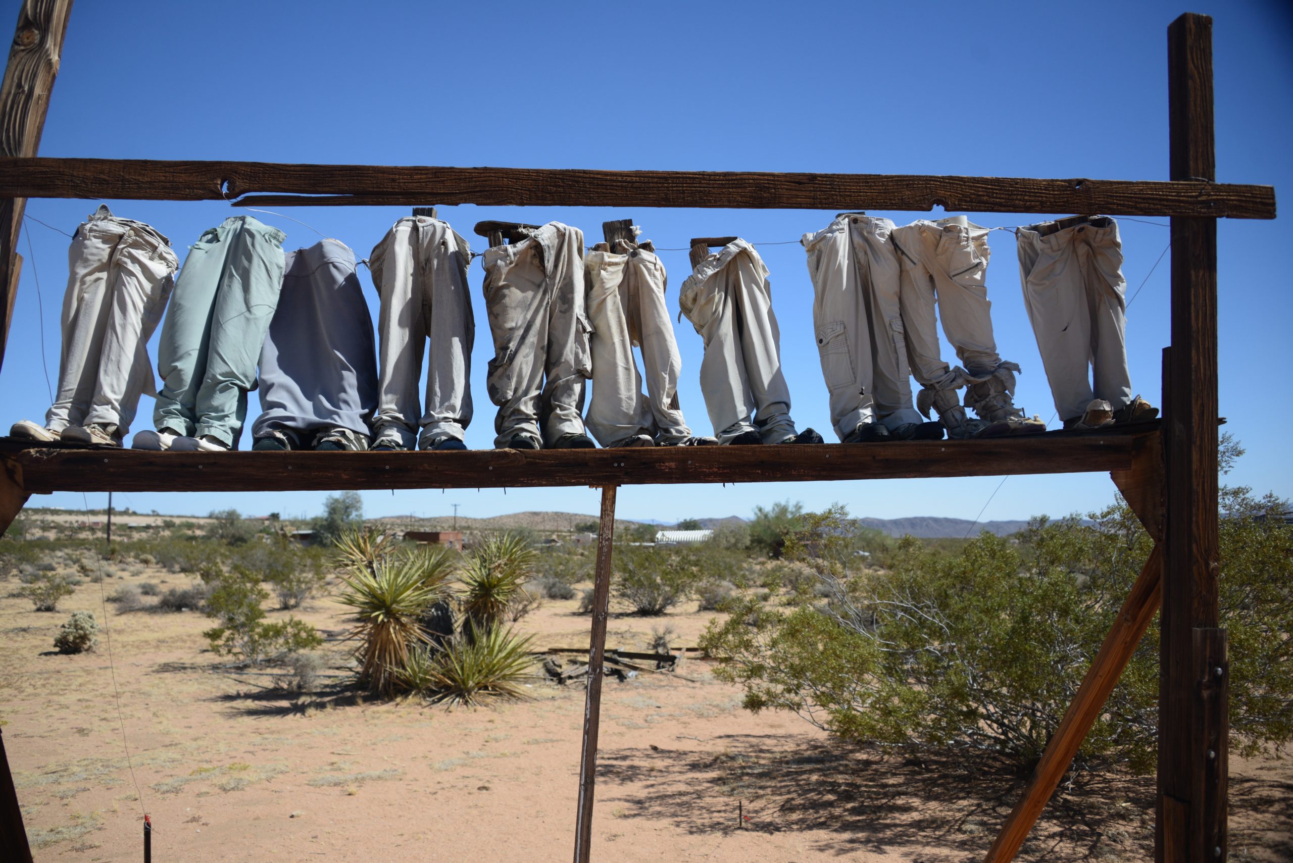 An art piece featuring a row of jeans and shoes hanging from a wooden rack in the desert.