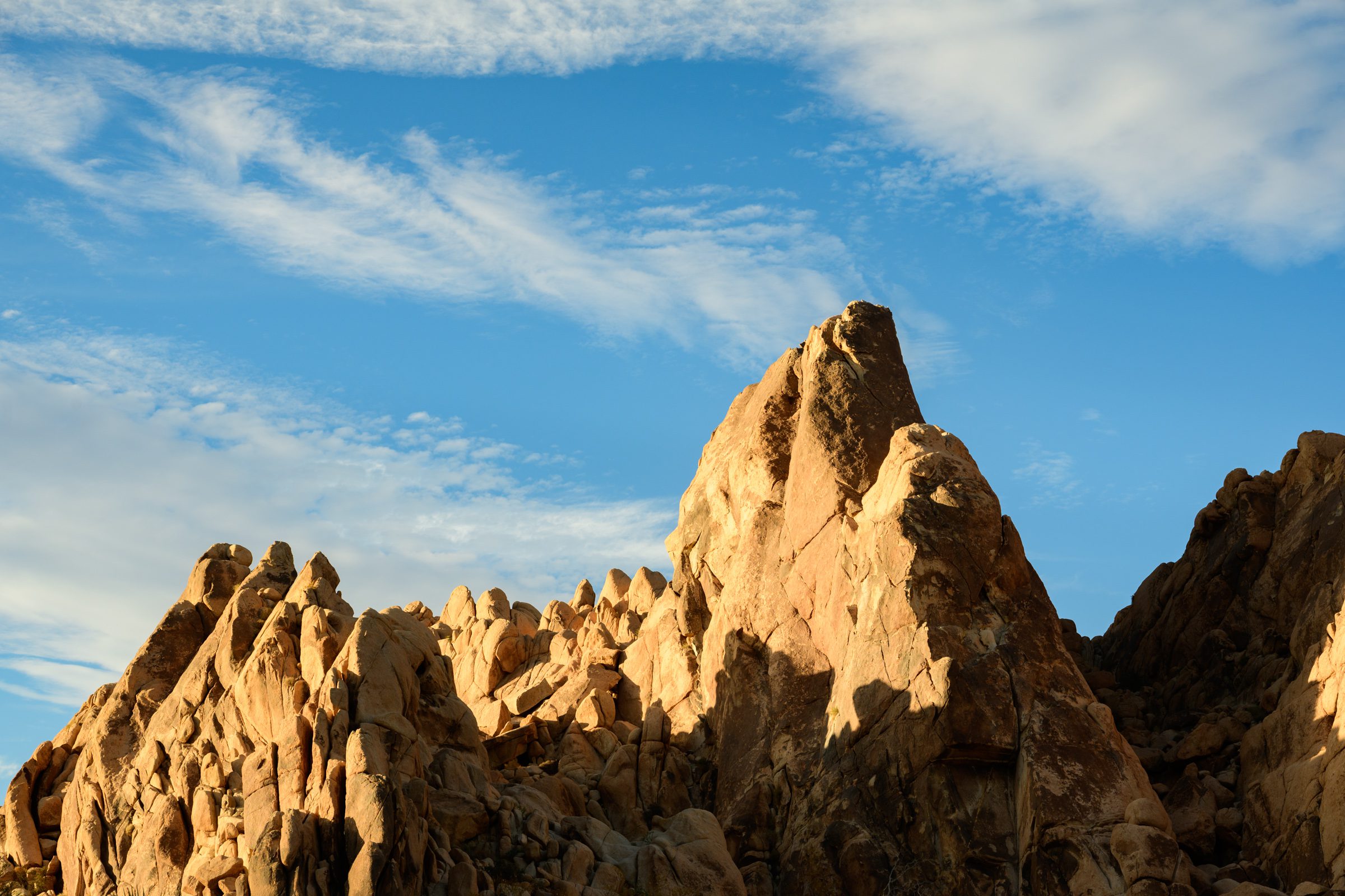 Rock formations at Joshua Tree National Park under a clear sky with wispy clouds.