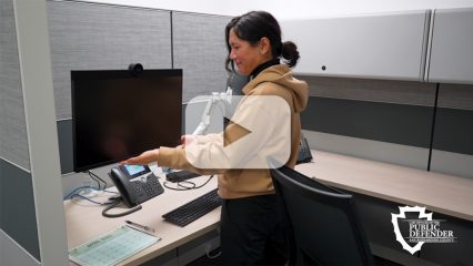 Public Service Employee adjusts computer monitor at cubicle in San Bernardino County Public Defender’s Office.