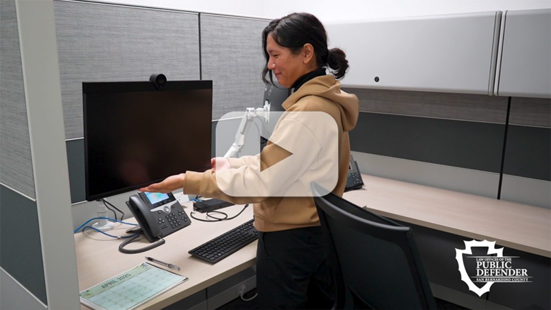 Public Service Employee adjusts computer monitor at cubicle in San Bernardino County Public Defender’s Office.