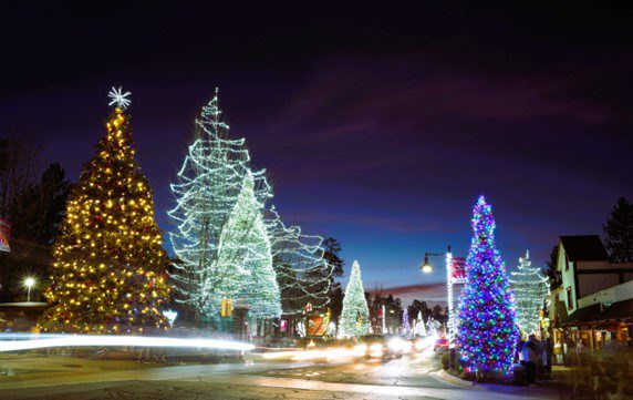 A view of a street in Big Bear Lake with multiple Christmas trees covered in colorful lights.