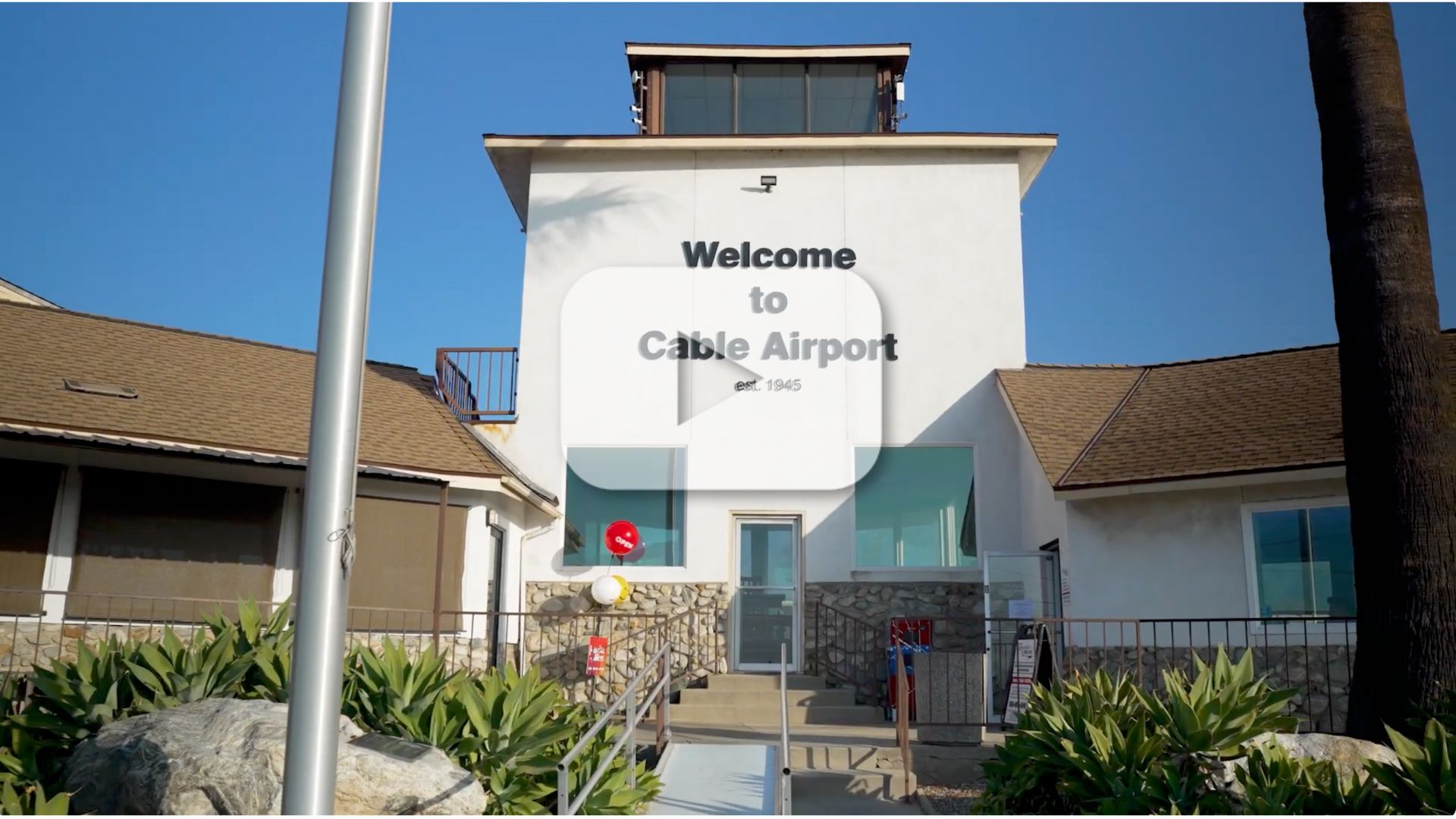 A shot of the "Welcome to Cable Airport" sign on a building with glass doors and windows.