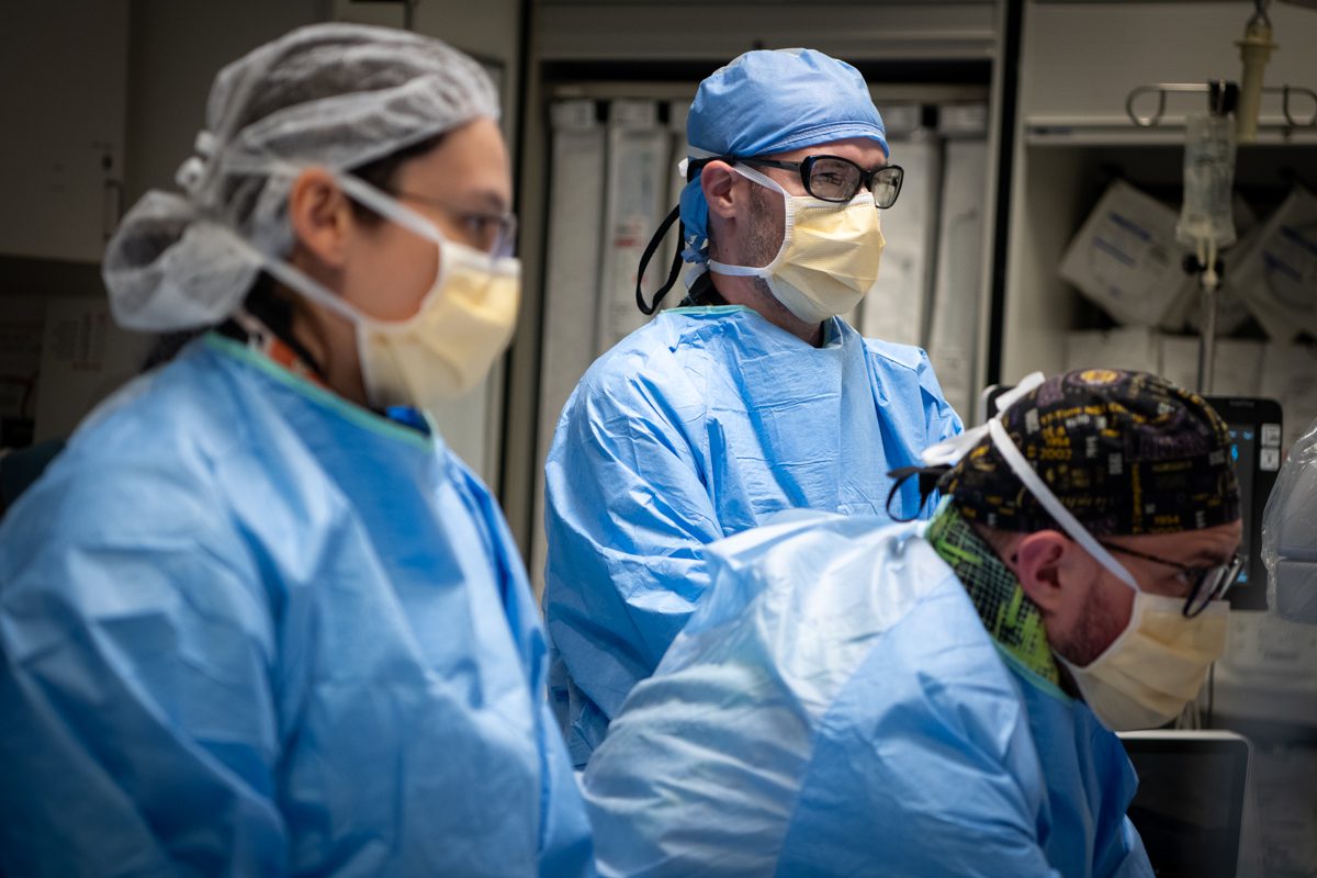 Healthcare professionals in an operating room, all wearing blue surgical gowns, masks and eyewear.