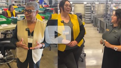 Election workers in yellow vests talk and as others in the background prepare ballots at a processing facility.