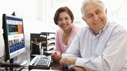A happy couple sits at a desk with a computer monitor showing the new website’s landing page.