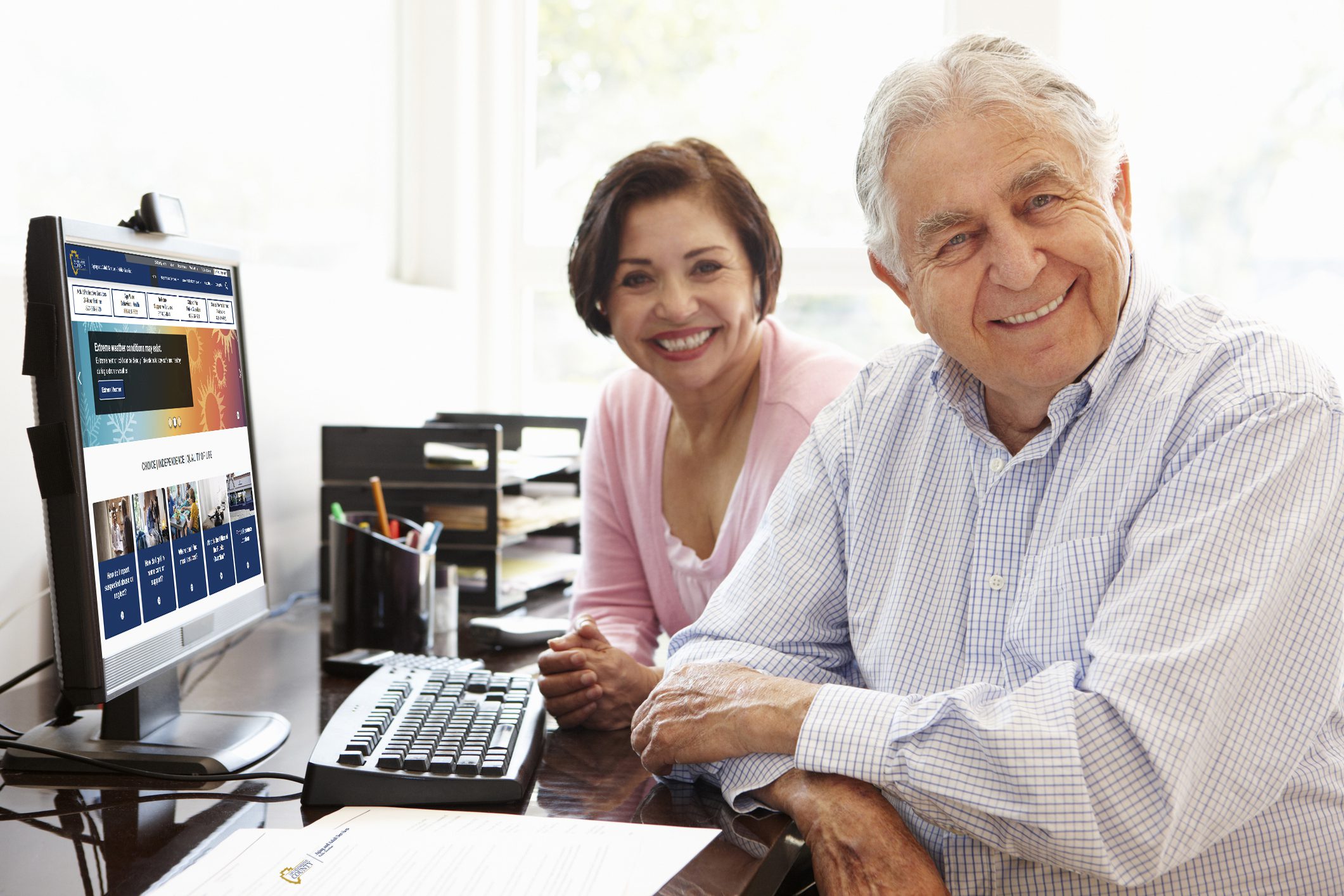 A happy couple sits at a desk with a computer monitor showing the new website’s landing page.