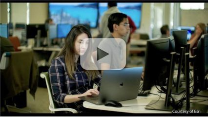 A person working on a laptop in a classroom environment with other individuals at desks using computers, courtesy of Esri.