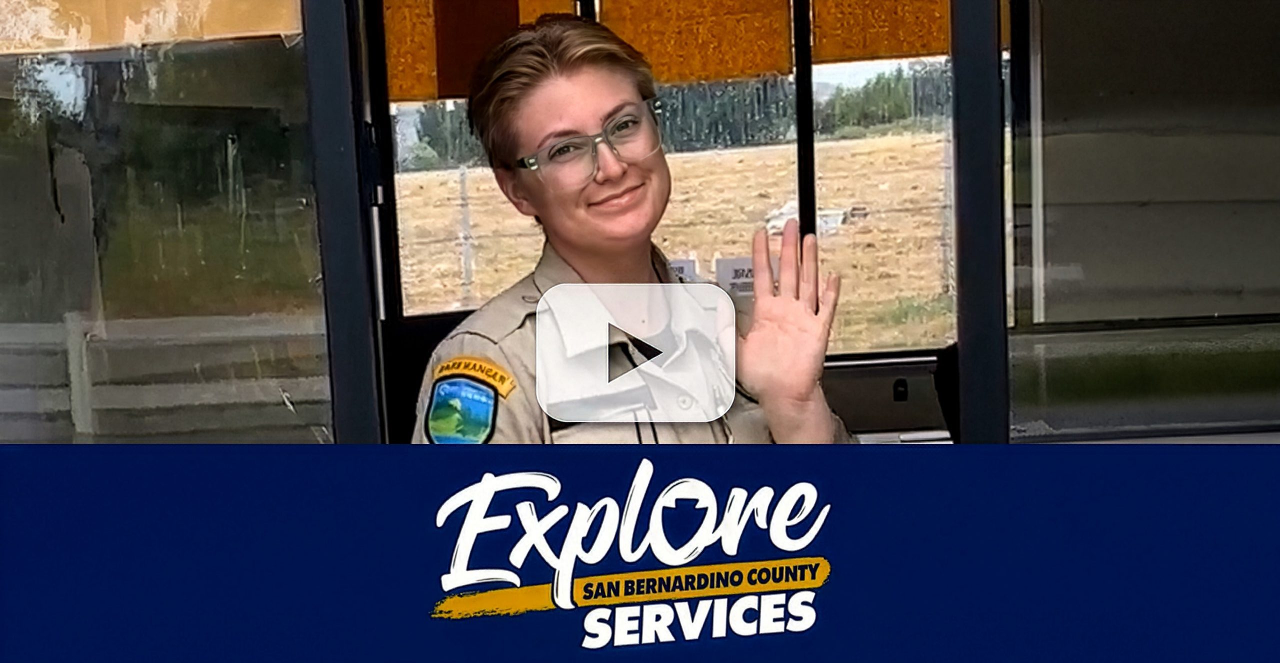 Park employee at entrance booth with "Explore San Bernardino County Services" campaign logo.
