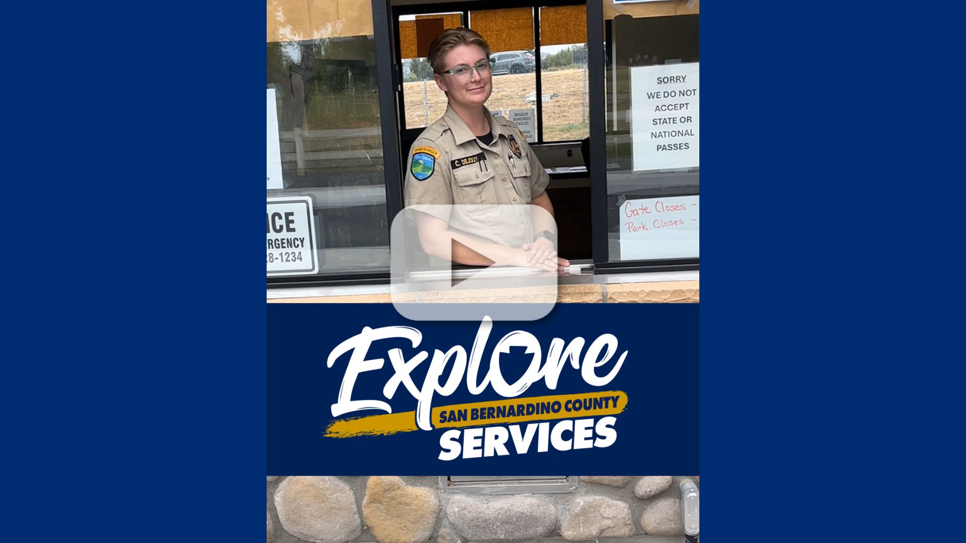 Park employee at entrance booth with "Explore San Bernardino County Services" campaign logo.