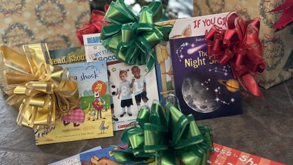 Children’s books with colorful bows under a Christmas tree.