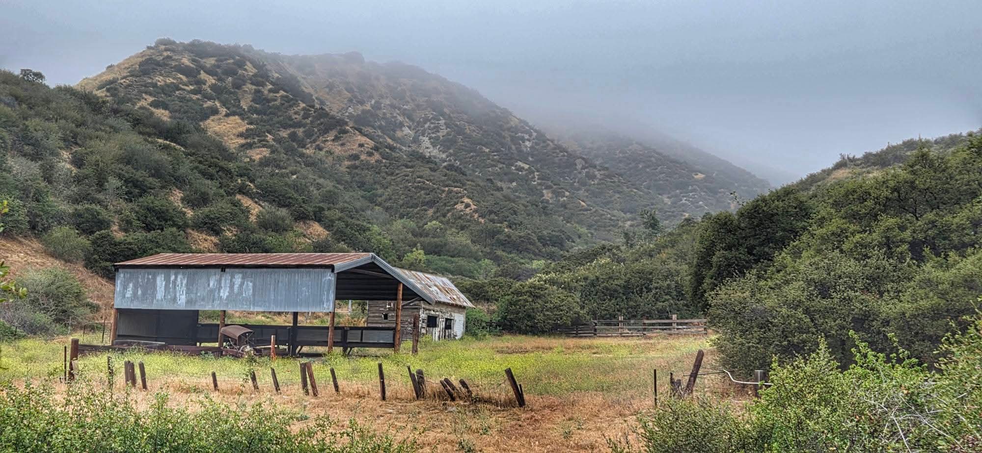 A barn in a field is surrounded by mountains.