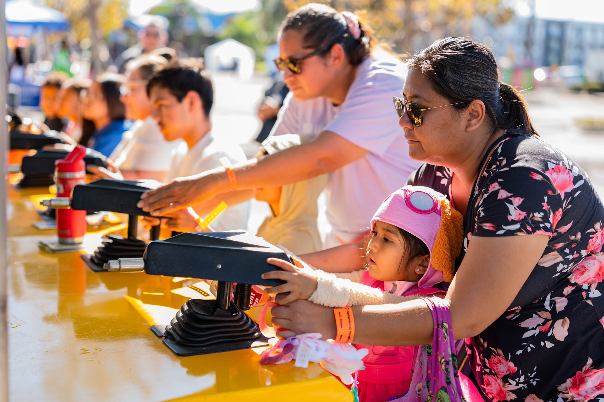 A young child, assisted by an adult, enjoys a carnival ride alongside other families at the Fall Wellness Extravaganza.