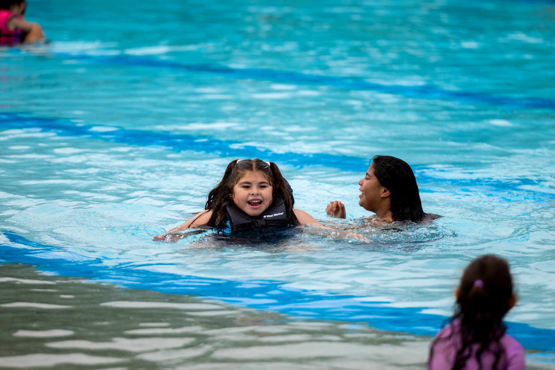 Three young girls are in a pool swimming.