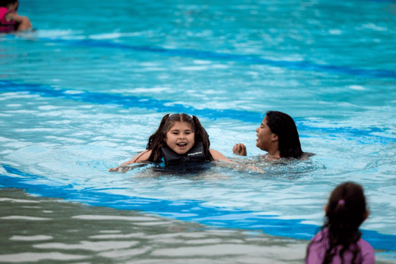 Three young girls are in a pool swimming.