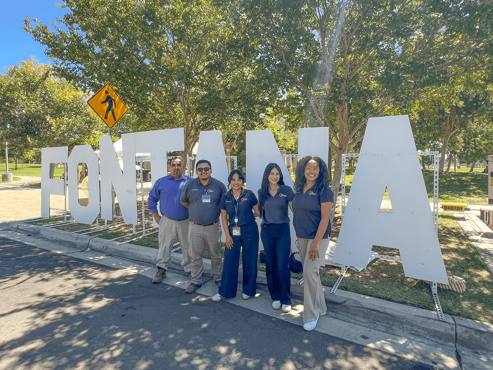 Healthy Communities Initiative staff and city of Fontana partners stand together outdoors near large city letter signage during a community meeting.