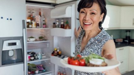 A woman stands by an open refrigerator holding a plate of nutritious food.