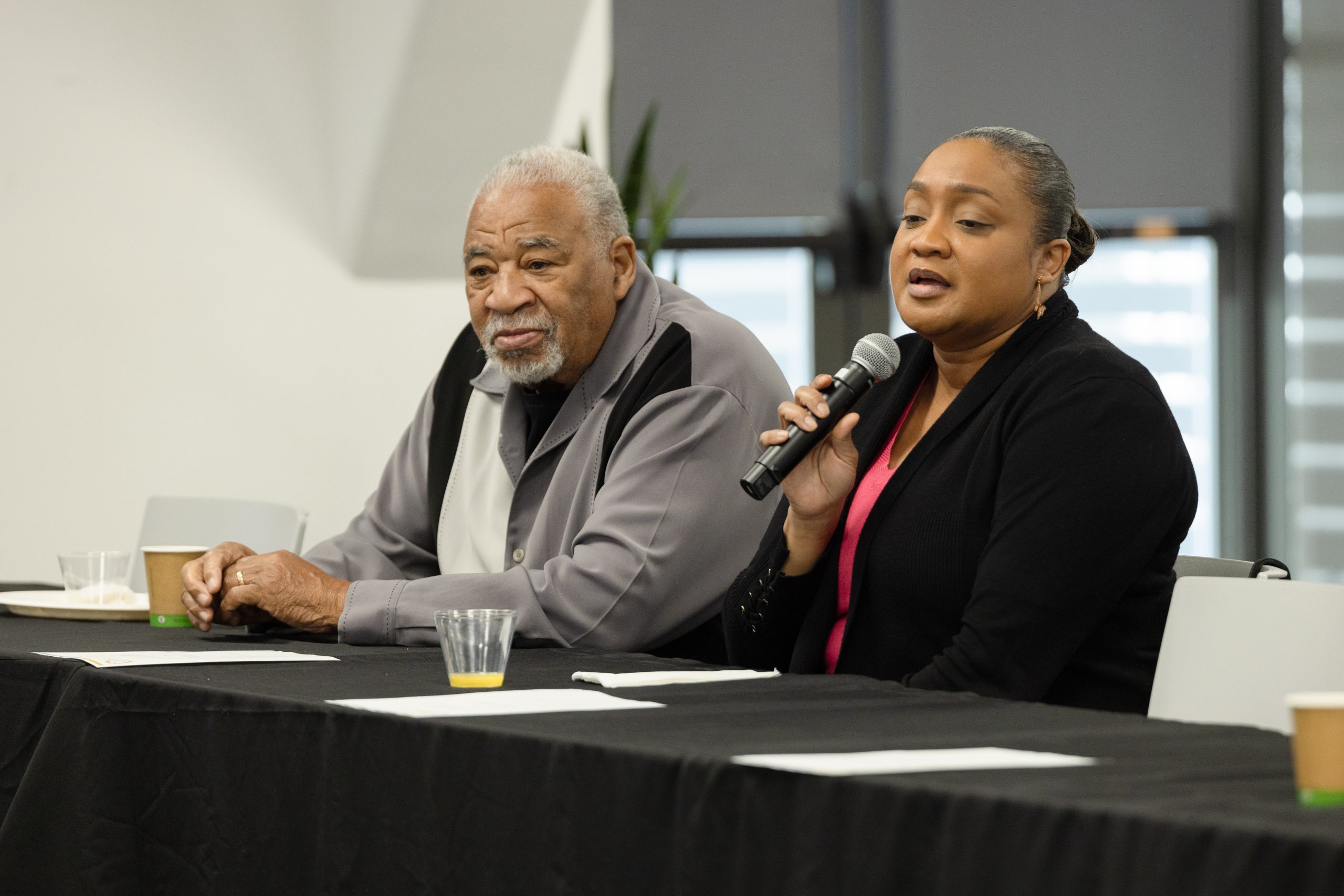 Woman with a microphone speaks while seated next to a colleague.