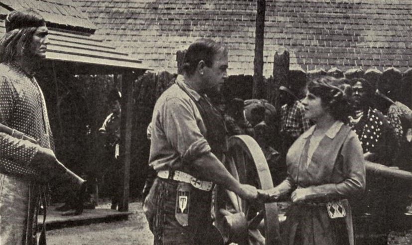 A scene from "The Call of the North" shows two people engaged in conversation while others observe.