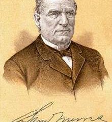 An image of an individual wearing a formal suit with a bow tie. The background is a warm brown color, and there is a signature at the bottom of the image.