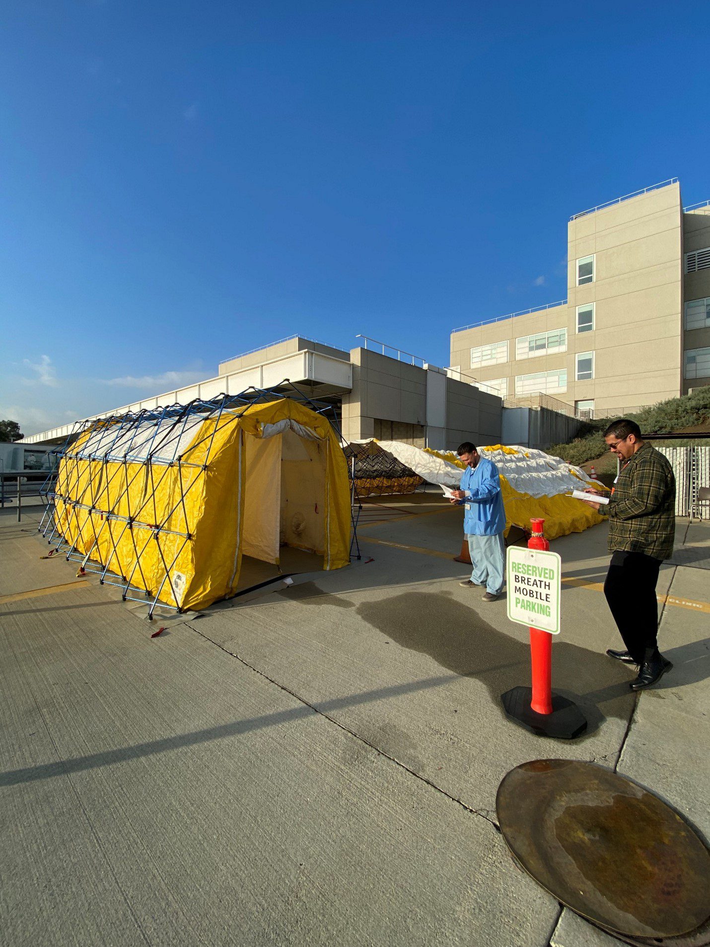 Two people with clipboards observe the set up of a medical modular shelter.