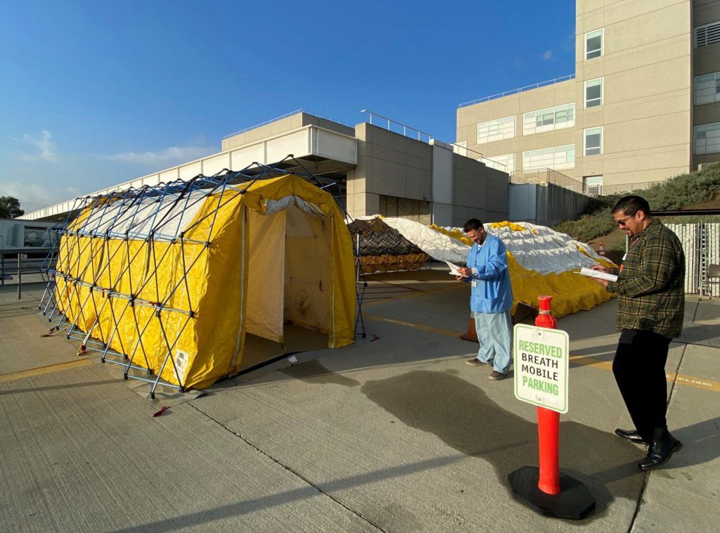 Two people with clipboards observe the set up of a medical modular shelter.