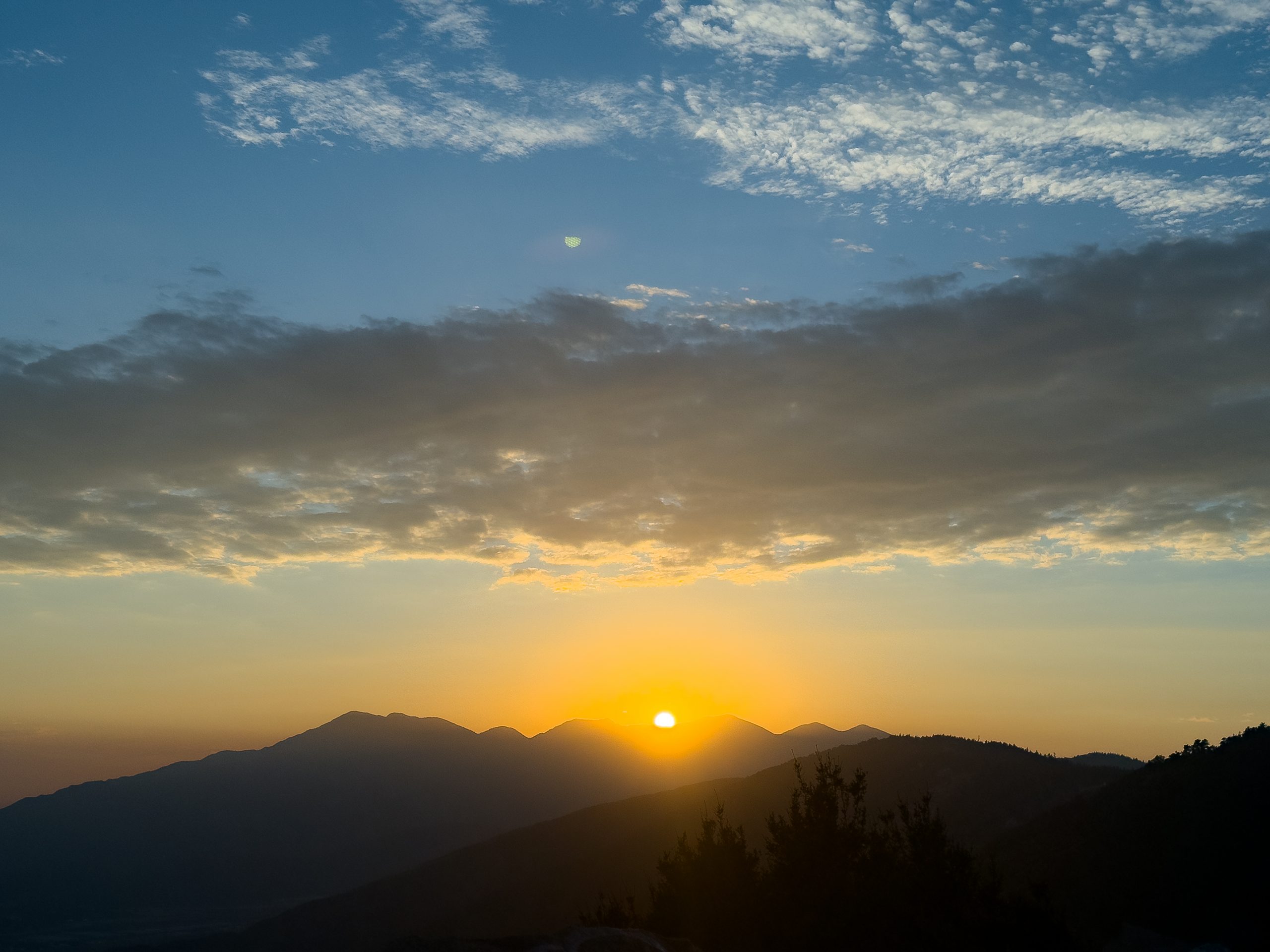 Sunset over mountainous landscape with speaks and a cloudy sky.