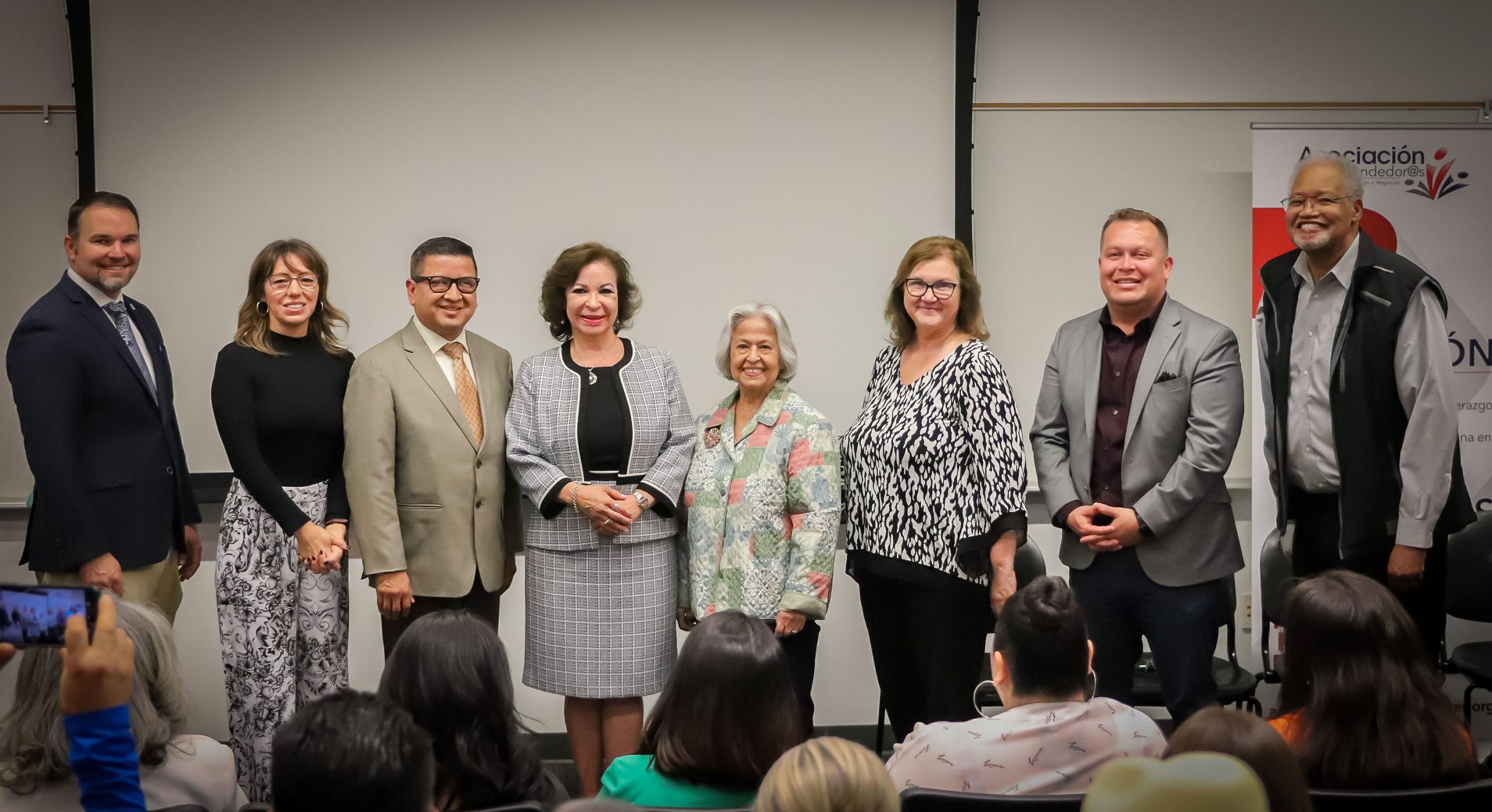 Eight people stand in a row smiling at an event hosted by Asociación de Emprendedor@s.