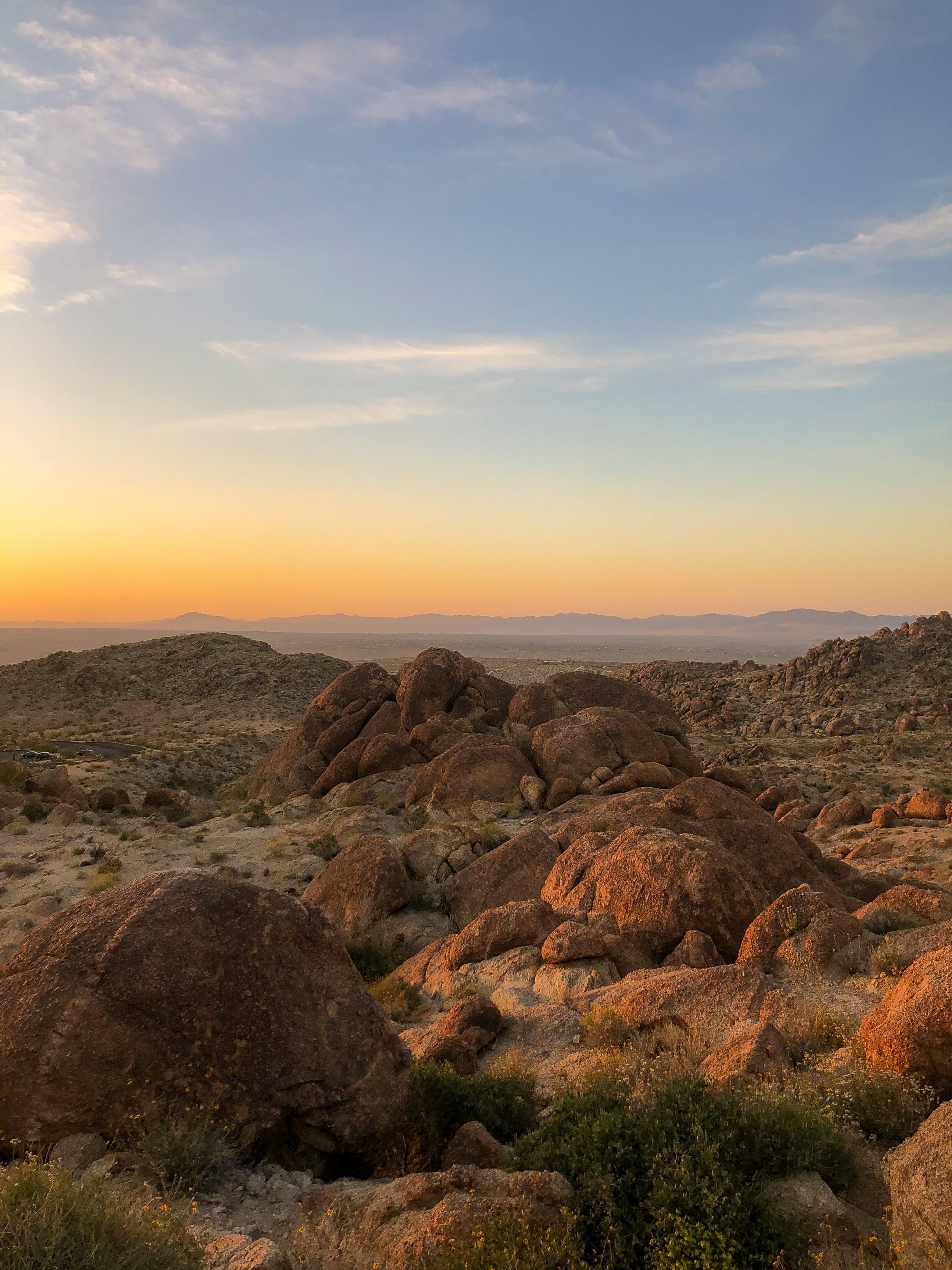 Sunset view at Joshua Tree National Park with large rocks in the foreground and mountains in the background.