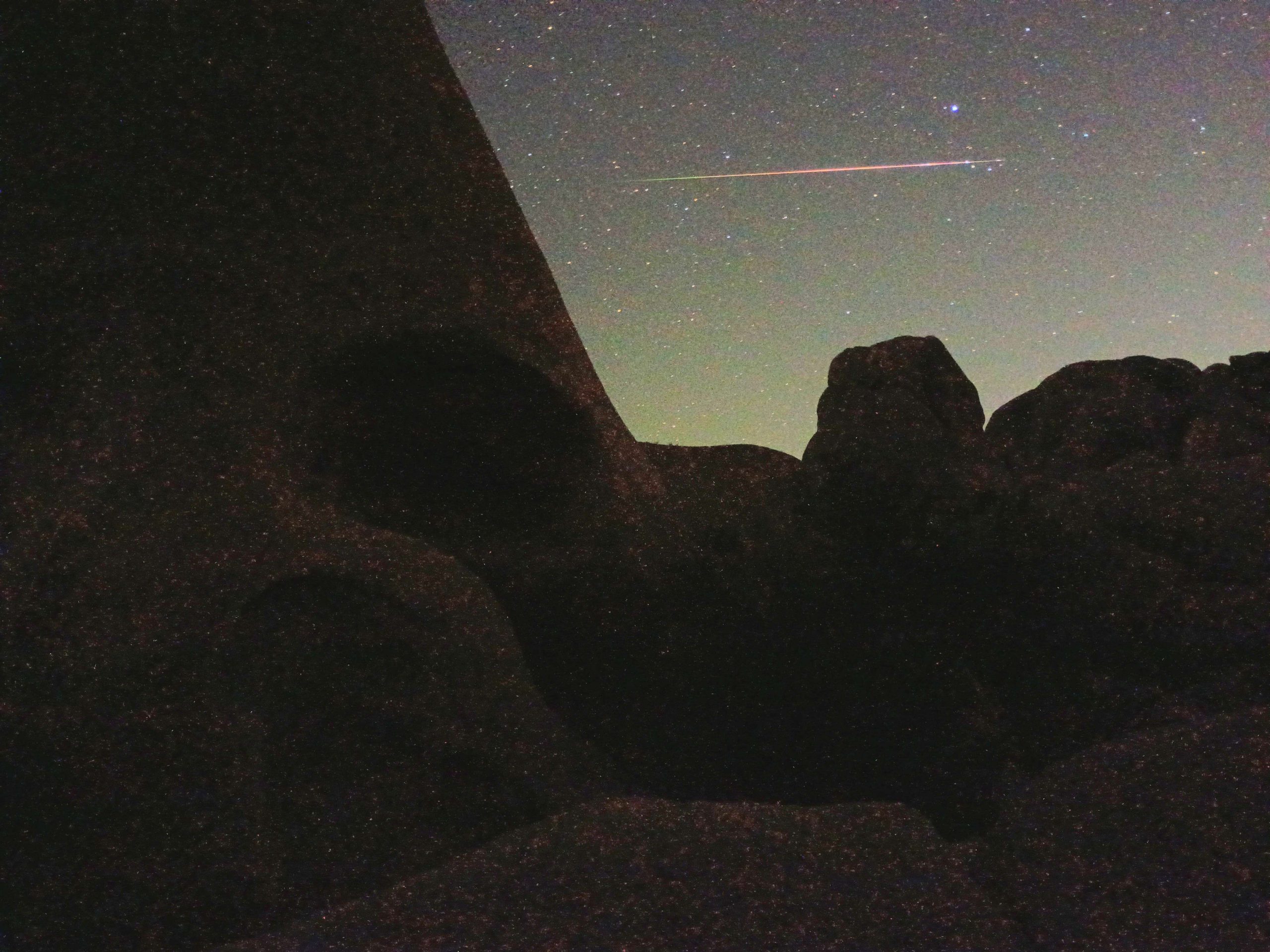 A starry night sky with a meteor streaking across it over a rocky landscape.