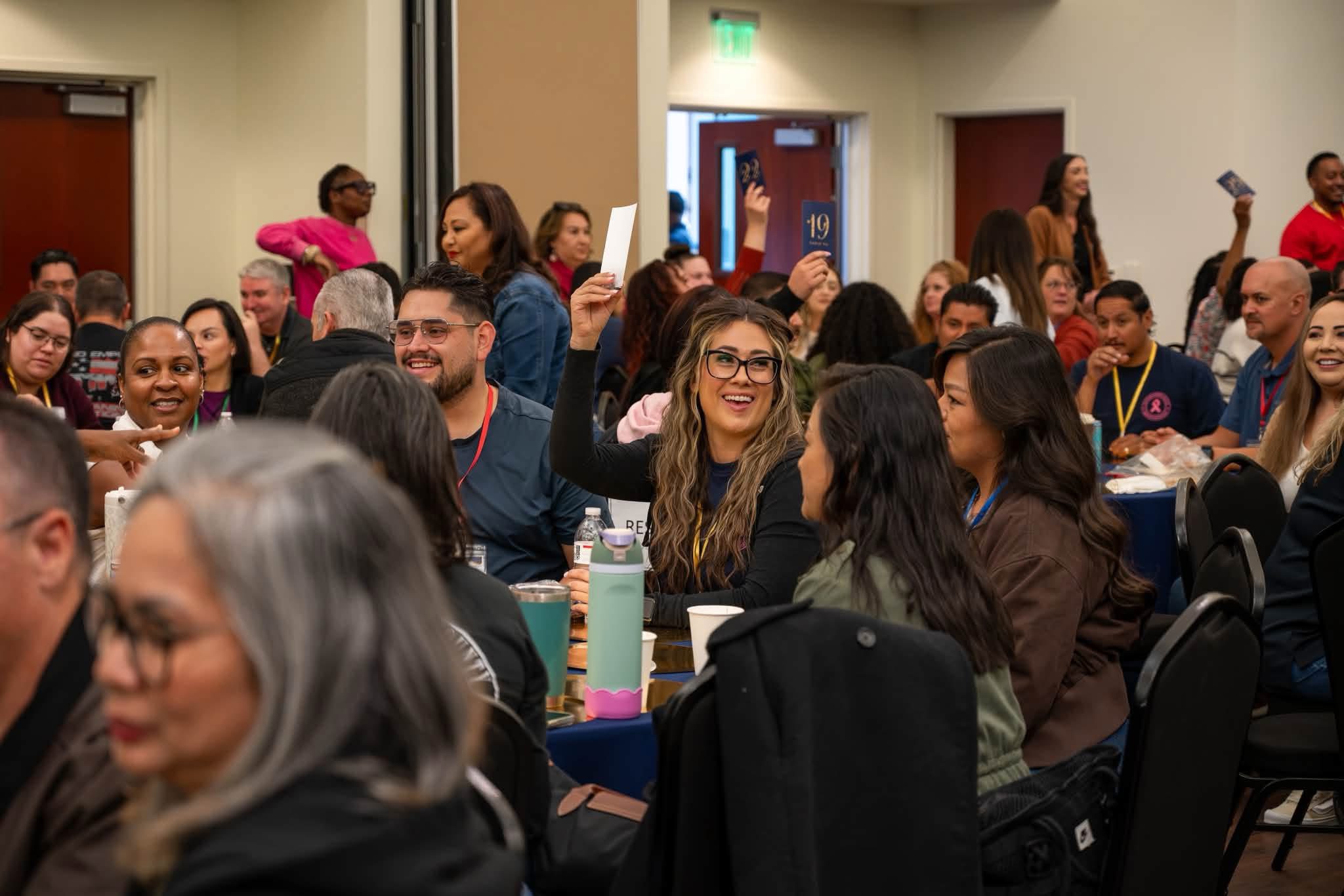 Employees smile and raise cards during an interactive activity at the State of the Department.