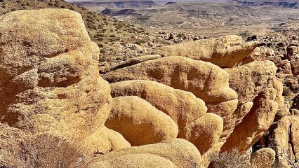Large rock formations in the foreground with the desert landscape and mountains in the background.