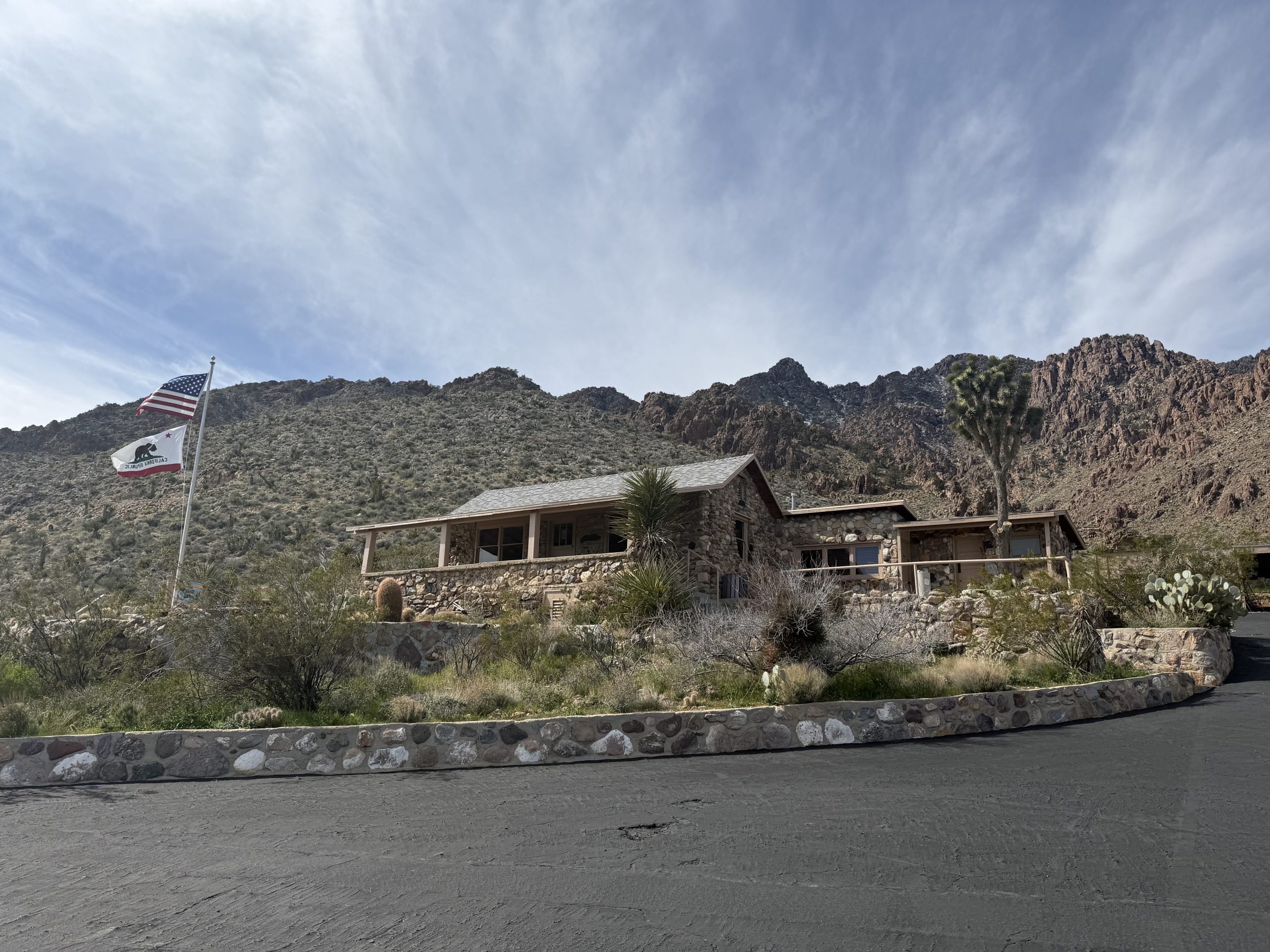 A stone building with mountain in the background. In the foreground, a pole displays the United States and California flags.