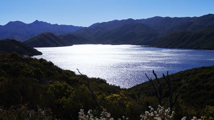 A large lake surrounded by mountains under a clear blue sky.