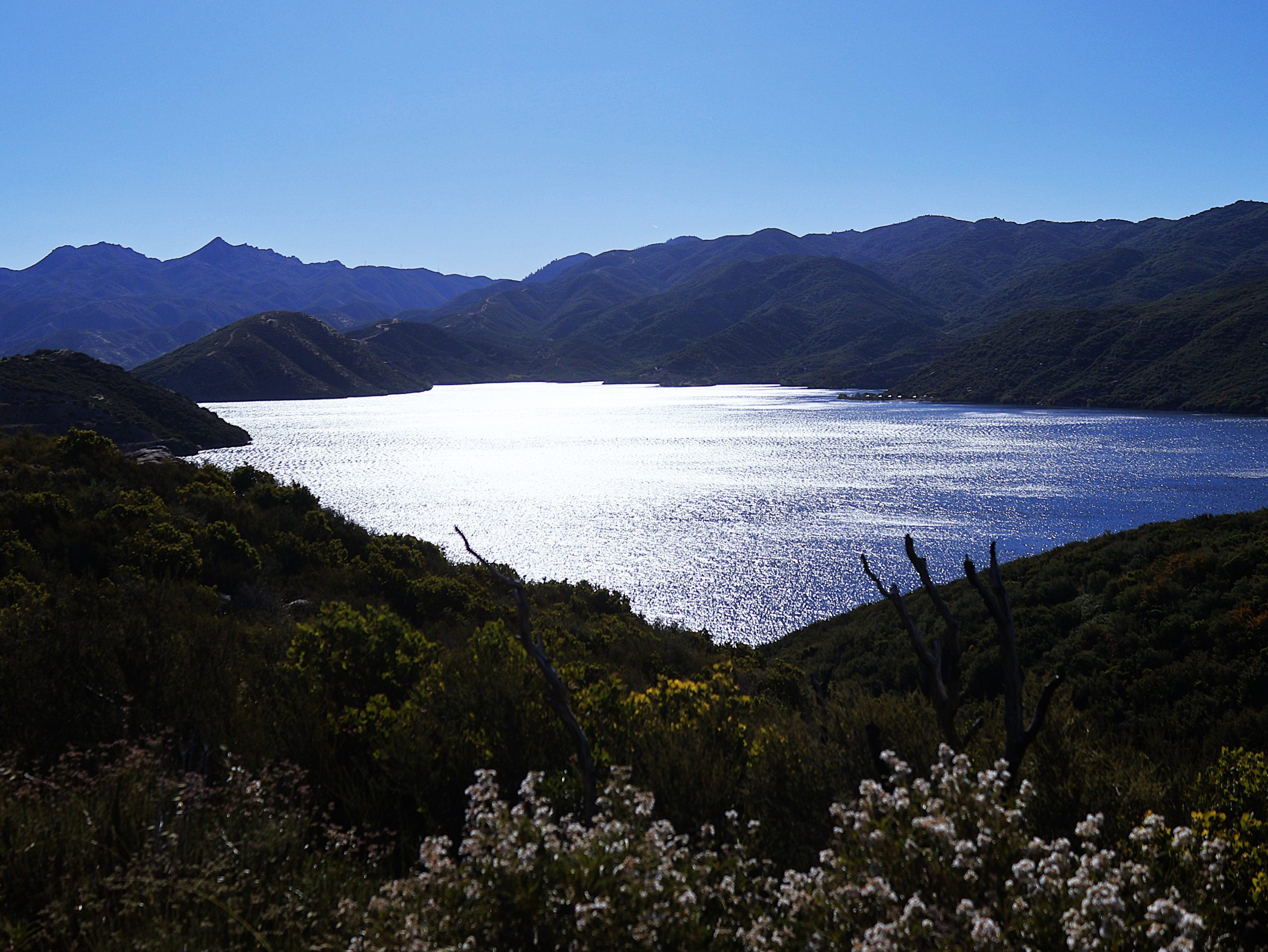 A large lake surrounded by mountains under a clear blue sky.
